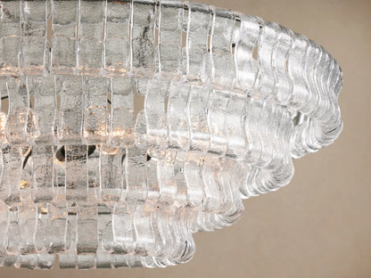 Angled view of Ghiaccio Round Chandelier. Clear, textured glass pieces form layered, wavy rings, glowing with warm light.