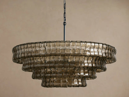 Tiered Ghiaccio Round Chandelier made of smoky, textured curved glass, suspended by a dark chain against a beige wall.