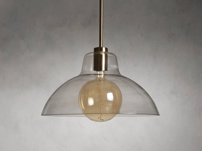 Bauer Dome Pendant with a transparent glass shade showcasing a glowing LED G200 bulb and brass finish, suspended by a rod.