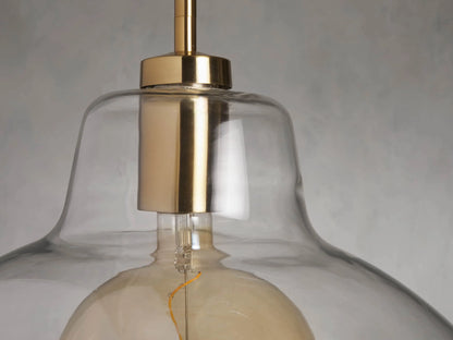 Bauer Dome Pendant with clear glass dome and visible LED bulb, brass finish, suspended from a pole against a neutral background.