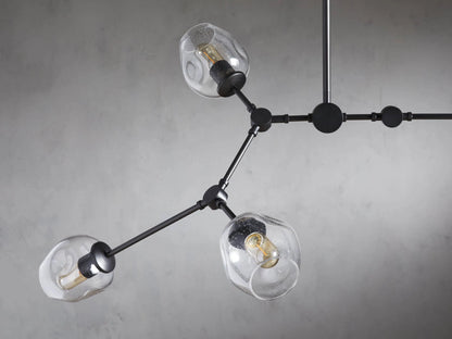 Noella Bronze Chandelier with five clear glass bulb holders on a bronze metal frame, hanging against a light gray wall.