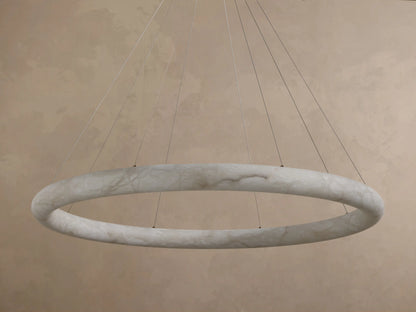 Front view of an illuminated Alabaster Ring Pendant Light, glowing warm white, revealing creamy translucent material with swirling veins.