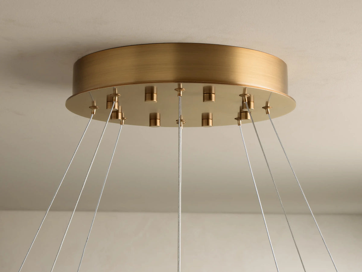 Close-up of ring pendant light with warm glowing, veined alabaster diffuser and bronze-toned metal frame, suspended by wires.