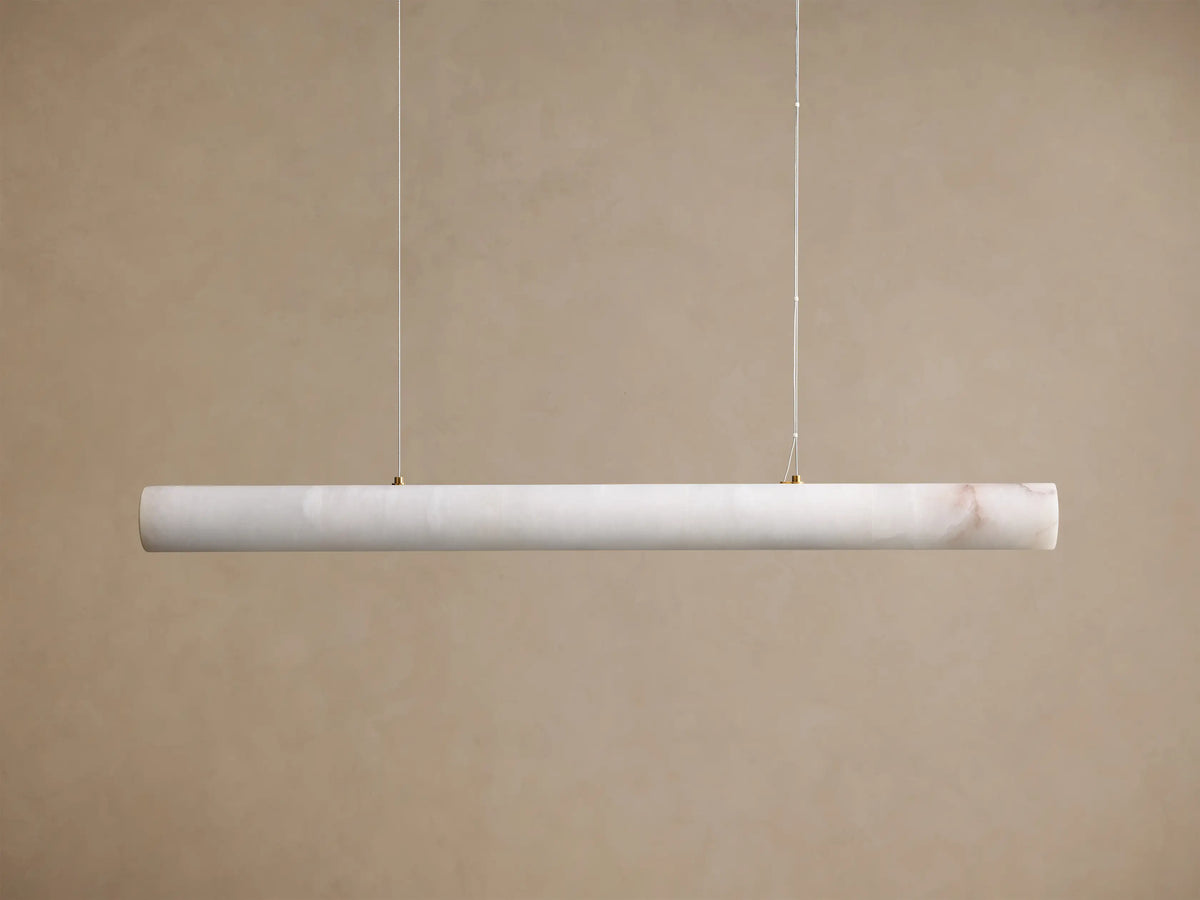 Translucent off-white onyx linear pendant light, glowing warmly with visible brown veining, suspended by thin wires.