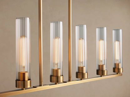 Andreas Linear Chandelier with 7 clear glass cylindrical shades and exposed filament bulbs on a brass bar, suspended by chains.