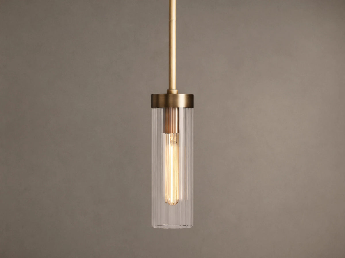 Brass Andreas Pendant with clear ribbed glass shade & illuminated filament bulb, hanging vertically against a neutral wall.