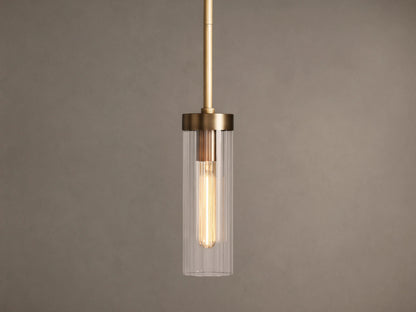 Brass Andreas Pendant with clear ribbed glass shade & illuminated filament bulb, hanging vertically against a neutral wall.
