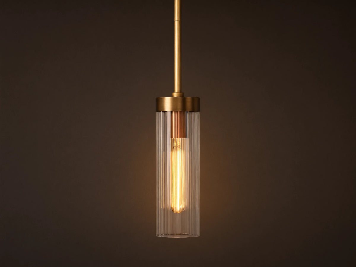 Brass Andreas Pendant with clear ribbed glass shade & illuminated filament bulb, hanging vertically against a neutral wall.