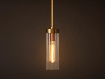 Brass Andreas Pendant with clear ribbed glass shade & illuminated filament bulb, hanging vertically against a neutral wall.