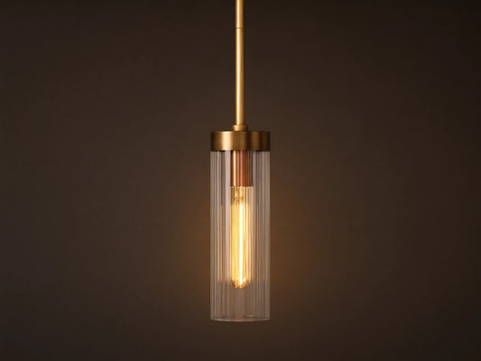Brass Andreas Pendant with clear ribbed glass shade & illuminated filament bulb, hanging vertically against a neutral wall.