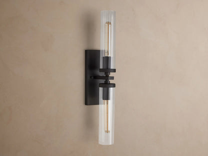 Andreas Double Sconce with two clear fluted glass shades, a dark bronze frame, and glowing exposed filament bulbs.