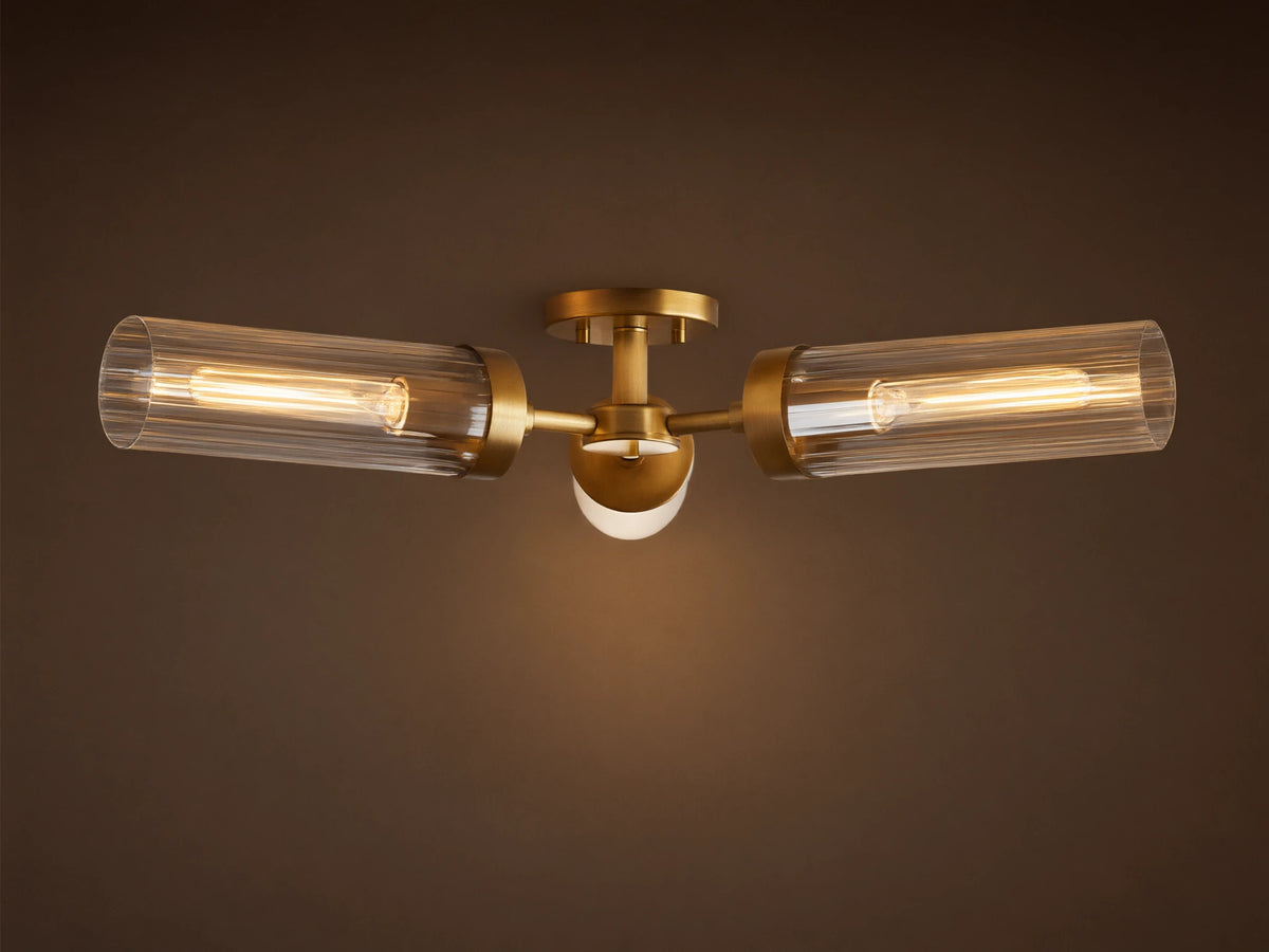 Andreas Flush Mount. Plated brass fixture with two horizontal ribbed glass cylinders, glowing filament bulbs, and small central light.