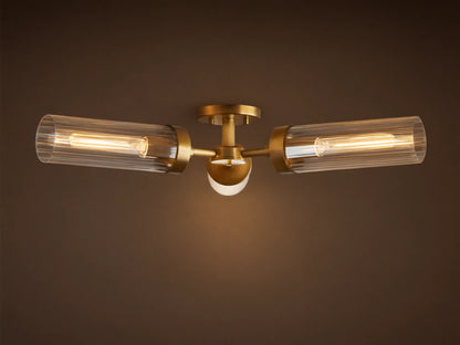 Andreas Flush Mount. Plated brass fixture with two horizontal ribbed glass cylinders, glowing filament bulbs, and small central light.