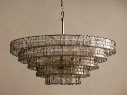 Ghiaccio Round Chandelier featuring tiered, textured smoky glass layers, suspended by a brass chain against a neutral wall.