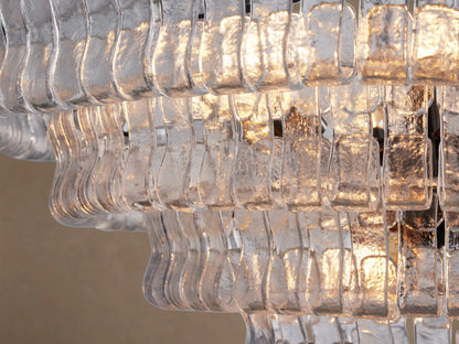 Close-up of Ghiaccio Round Chandelier with multiple layers of textured, curved clear glass panels glowing with warm light.