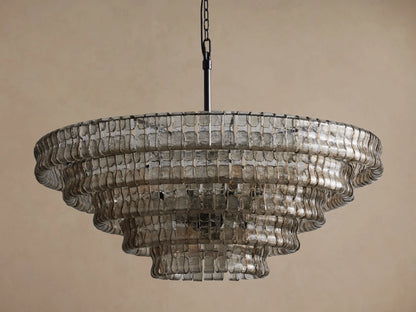 Ghiaccio Round Chandelier, tiered, composed of wavy, rectangular clear glass pieces, suspended from a black chain against a beige wall.