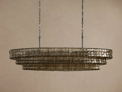 Ghiaccio Oval Chandelier with three tiers of textured, wavy, smoky glass panels, suspended by dark chains, glowing warmly.