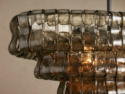 Ghiaccio Oval Chandelier features multiple layers of wavy, smoky brown glass panels, suspended by dark metal chains.