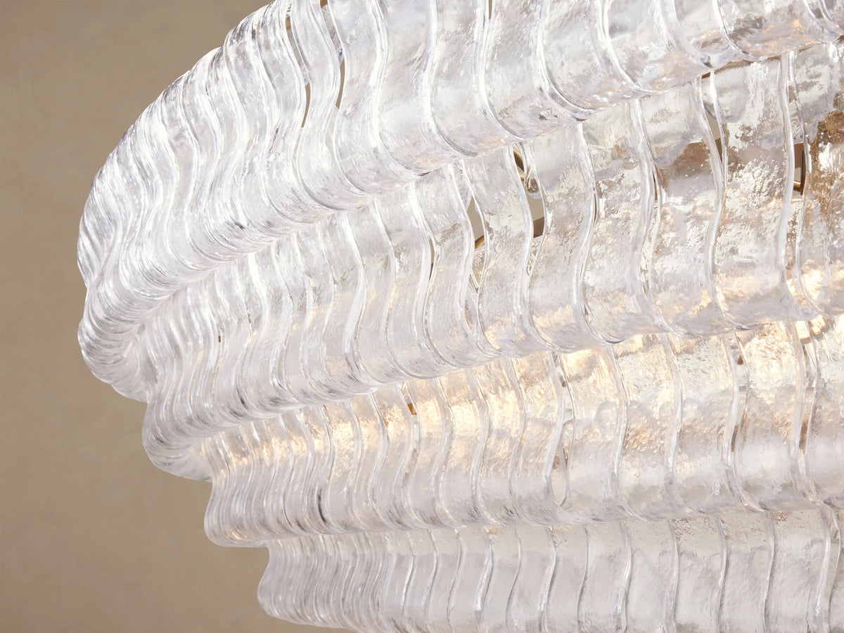 Ghiaccio Oval Chandelier: layered clear textured glass in an oval shape, suspended by two gold chains against a beige wall.