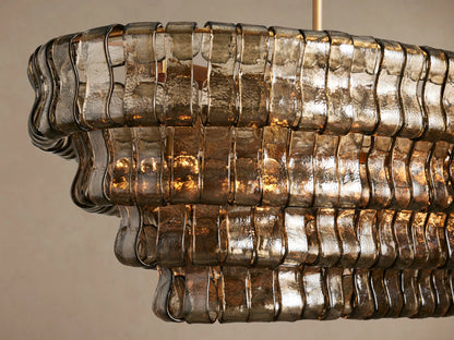Ghiaccio Oval Chandelier with multi-tiered, textured smoky glass panels. Suspended by two gold chains against a neutral background.