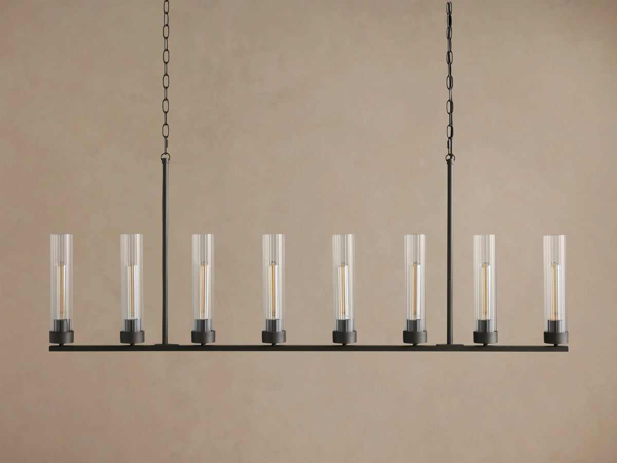 Andreas Linear Chandelier with 8 clear fluted glass shades, dark bronze frame, and warm glowing filament bulbs, hanging from chains.