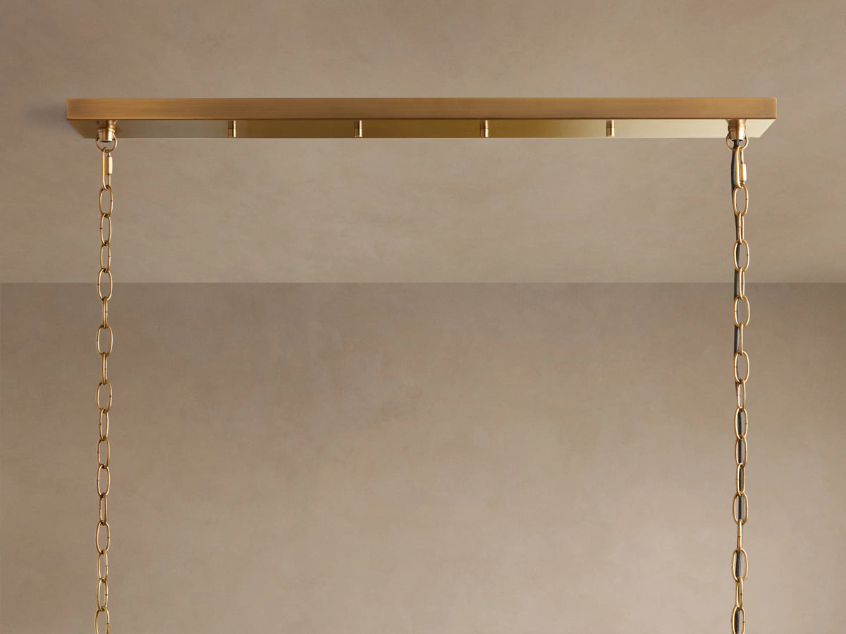 Andreas Linear Chandelier, close-up of five clear fluted glass shades with warm glowing bulbs on a horizontal brass bar, angled up.