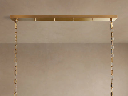 Andreas Linear Chandelier, close-up of five clear fluted glass shades with warm glowing bulbs on a horizontal brass bar, angled up.