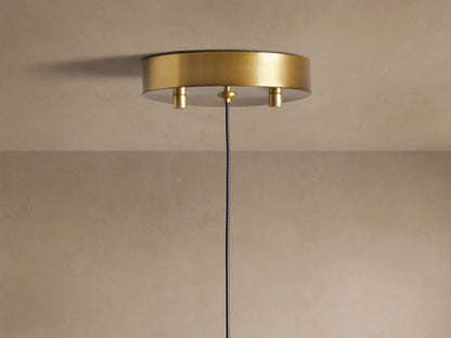Soltaire Pendant: Close-up of a brass-topped, clear teardrop glass pendant light with illuminated bubbles inside, glowing warmly.