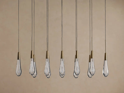 Soltaire Linear Chandelier: Multiple clear bubbled teardrop glass pendants with conical brass tops, suspended by thin black cords.