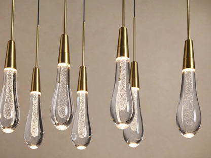 Soltaire Linear Chandelier with multiple teardrop clear glass pendants, brass-finished tops, and sparkling internal lights.