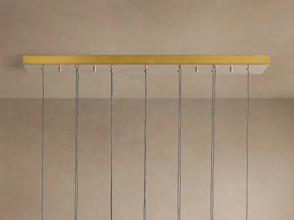 Soltaire Linear Chandelier showing its gold-finished linear canopy mounted to a light ceiling, with multiple black cords hanging.