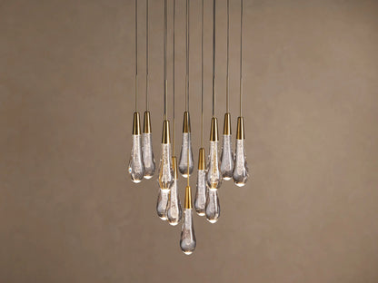 Soltaire chandelier with many illuminated teardrop glass pendants, brass caps, and internal bubbles, clustered against a neutral wall.