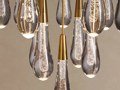 Close-up of Soltaire Round Chandelier showing multiple clear, bubbly teardrop glass pendants with brass tops, glowing brightly.