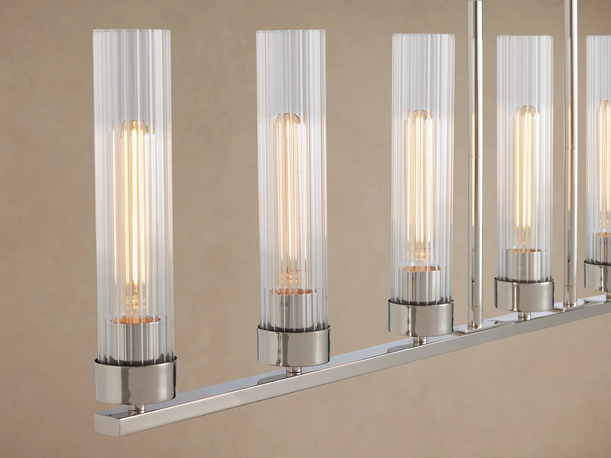 Andreas Linear Chandelier, polished nickel steel with 8 clear ribbed glass shades, hanging from two chains against a beige wall.