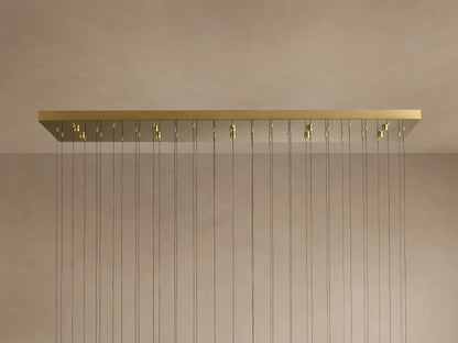 Soltaire Linear Chandelier: long brass rectangular canopy with many thin cords hanging down against a light beige wall.