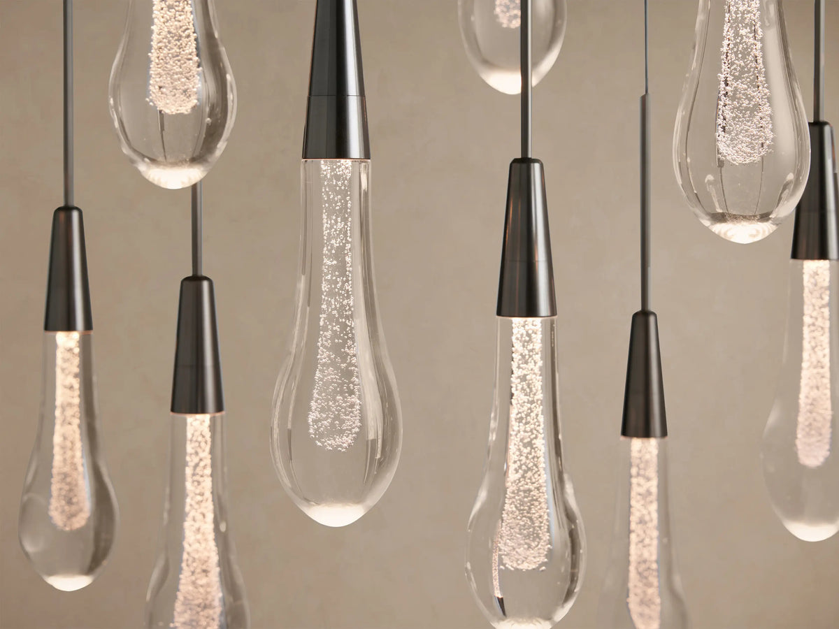 Soltaire Linear Chandelier: A close-up of multiple clear, tear-drop glass lights with sparkling internal LEDs and dark tapered caps.
