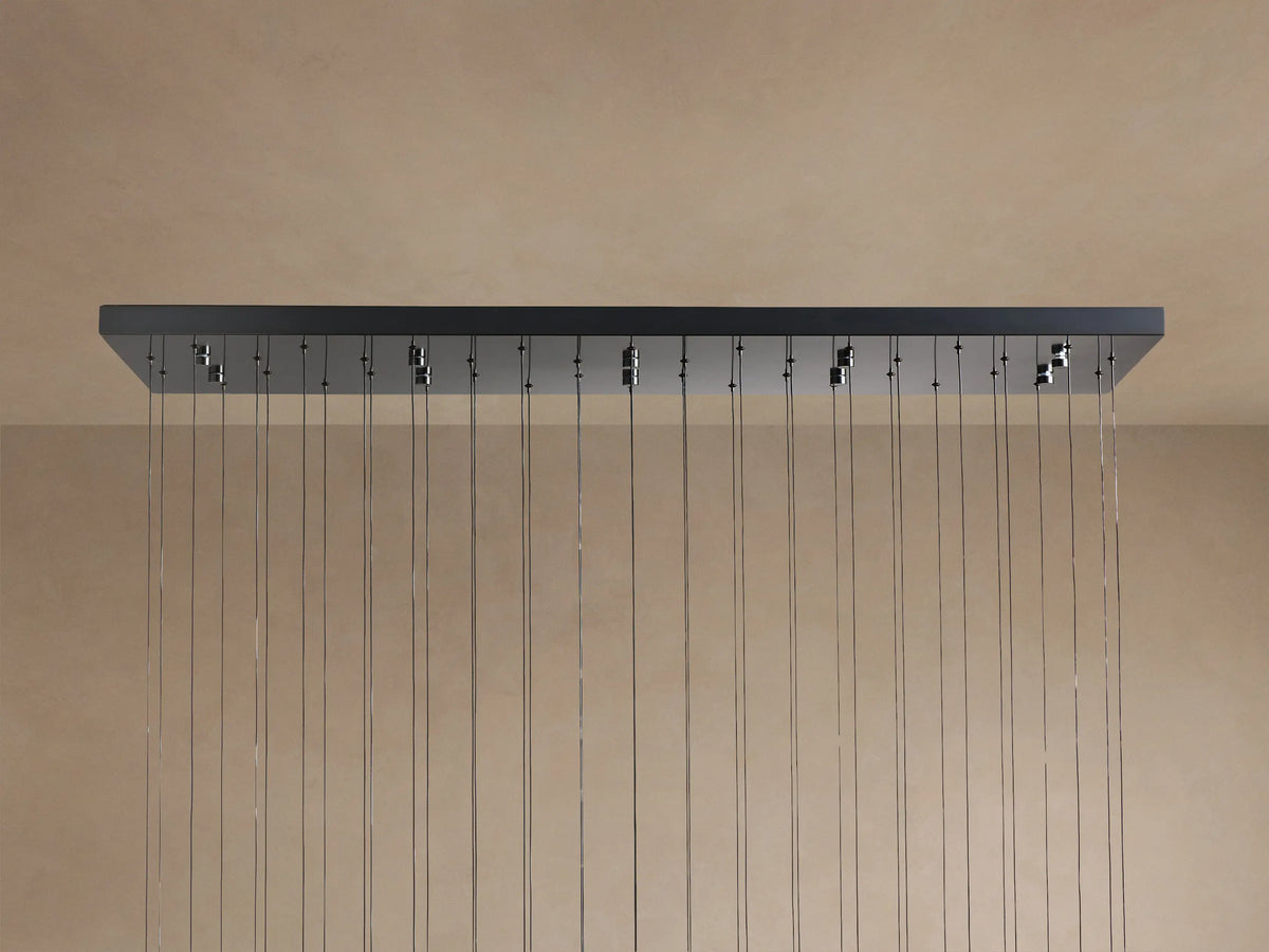 Soltaire Linear Chandelier with a dark rectangular canopy mounted to a light brown surface, featuring many thin hanging wires.