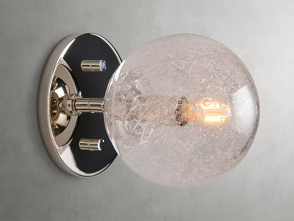 Mandoza Sconce with polished nickel-finished steel base featuring a textured hand-blown glass globe, mounted on a wall.