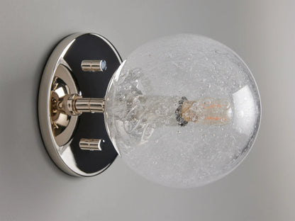 Mandoza Sconce with polished nickel-finished steel base featuring a textured hand-blown glass globe, mounted on a wall.