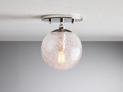 Mandoza Sconce with polished nickel-finished base, clear hand-blown glass globe, visible filament bulb, mounted on a wall.