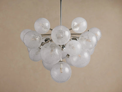 Mandoza Chandelier: Clustered, illuminated textured glass globes on a polished nickel frame, centered against a warm beige wall.