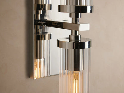 Andreas Double Sconce: polished nickel, two vertical clear ribbed glass shades, visible filament bulbs on a beige wall.