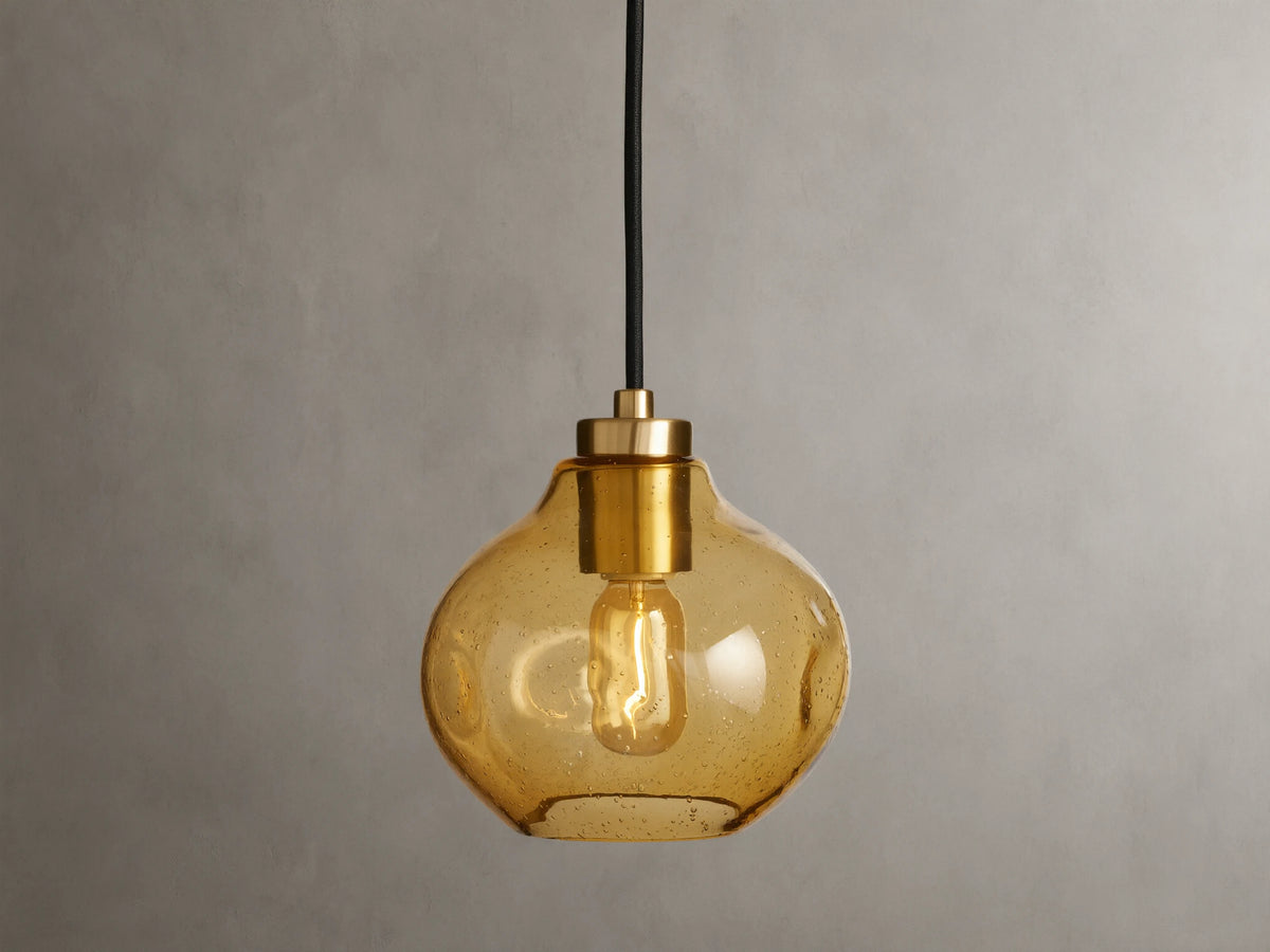 Organic 8" Pendant with amber mouth-blown glass shade, showing a visible filament bulb, suspended by a black fabric cord against a neutral background.