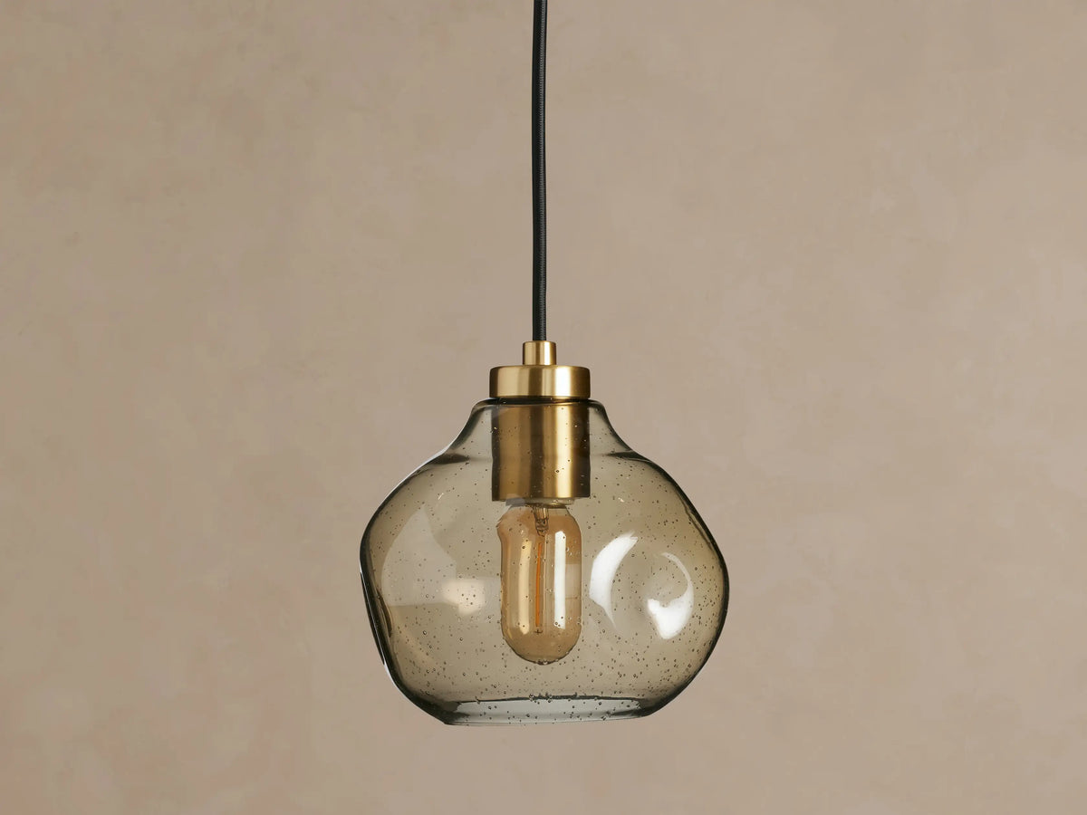 Organic 8" Pendant with a unique, smoky mouth-blown glass shade, brass fitting, black fabric cord, and glowing filament bulb.