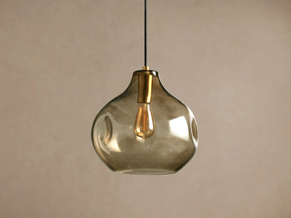 Organic 12" Pendant with smoky gray mouth-blown glass shade, brass fitting, glowing Edison bulb, black cord, hanging.
