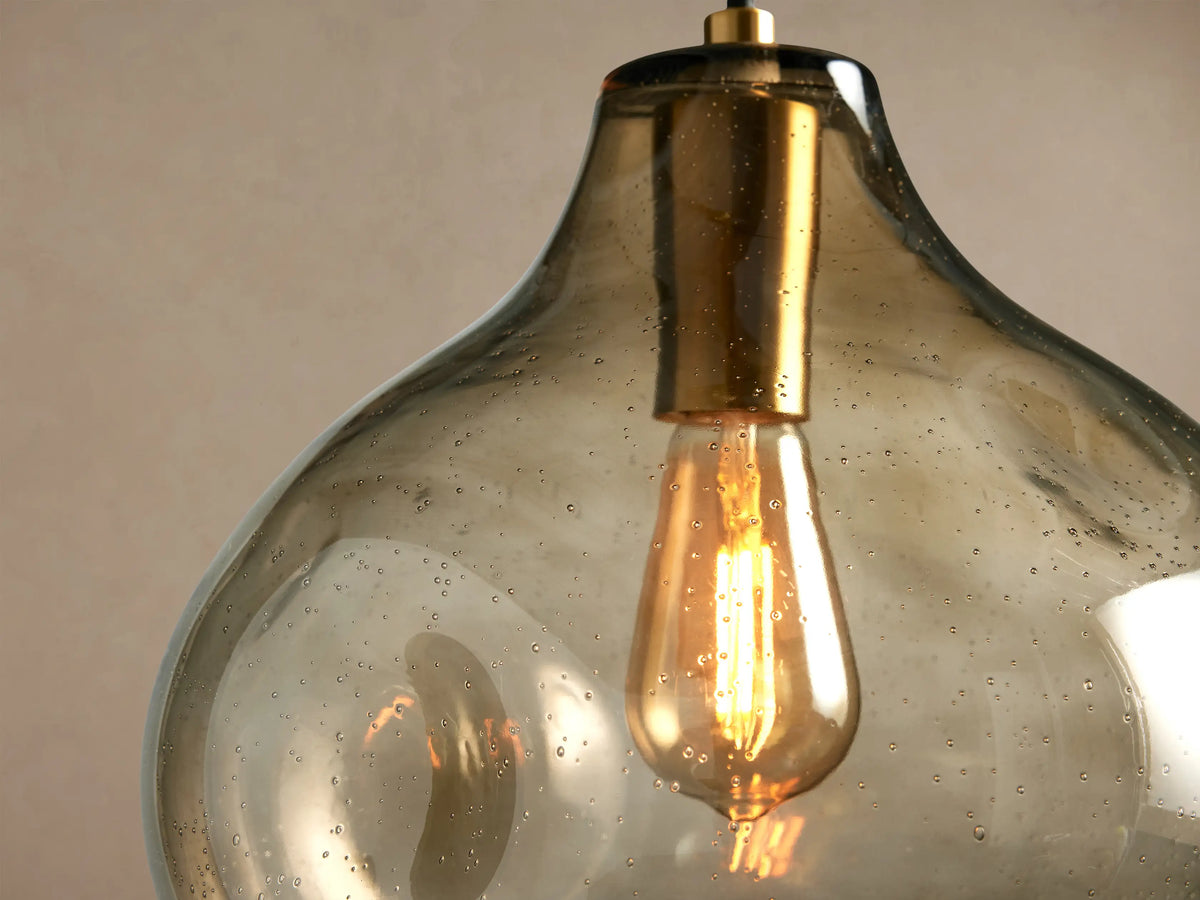 Close-up of an illuminated Organic 12" Pendant with amber seeded glass shade, gold fixture, and warm glow from a vintage bulb.