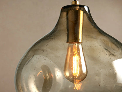 Close-up of an illuminated Organic 12" Pendant with amber seeded glass shade, gold fixture, and warm glow from a vintage bulb.