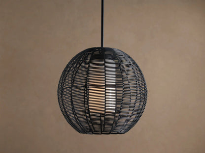 Cohen Globe Outdoor Pendant: Black woven wicker globe with an illuminated white inner shade, hanging from a dark pole against a brown wall.