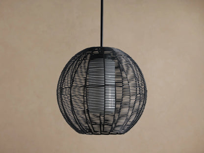 Cohen Globe Outdoor Pendant: Black woven wicker globe with an illuminated white inner shade, hanging from a dark pole against a brown wall.