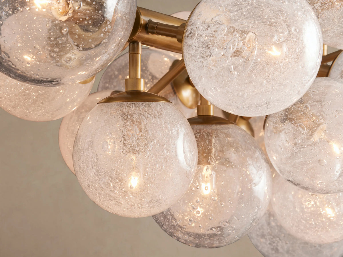 Mandoza Linear Chandelier: horizontal burnished brass bar with multiple textured clear glass globes, hanging against a beige wall.